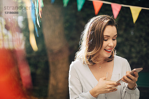 Lächelnde junge Frau benutzt Mobiltelefon  während sie im Hinterhof steht
