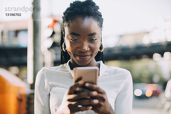 Junge Frau lächelt  während sie ein Smartphone auf der Straße in der Stadt benutzt