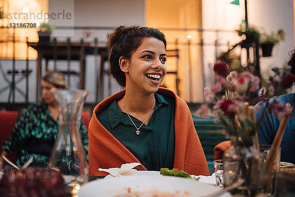 Lächelnde junge Frau schaut weg  während sie während der Dinnerparty am Tisch sitzt