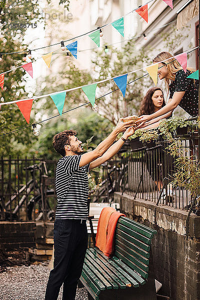 Junge Frau gibt lächelnden männlichen Freund während Gartenparty vom Balkon aus Essen