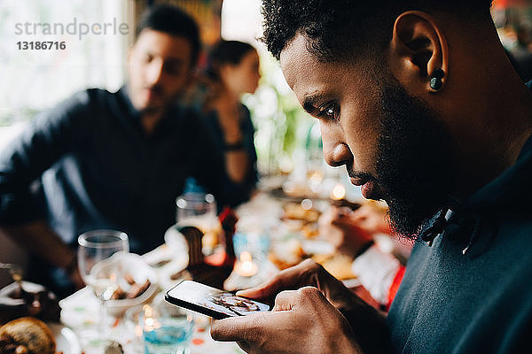 Junger Mann fotografiert Mittagessen  während er während einer Party mit Freunden im Restaurant sitzt