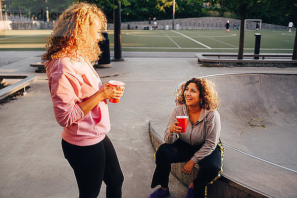 Lächelnde junge Frauen unterhalten sich bei einem Drink im Skateboard-Park
