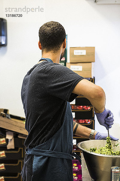 Seitenansicht eines jungen männlichen Kochs bei der Zubereitung von Speisen in einem Container in einer Großküche