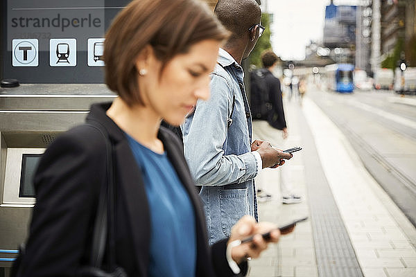 Pendler mit Smartphone beim Warten auf dem Bürgersteig in der Stadt