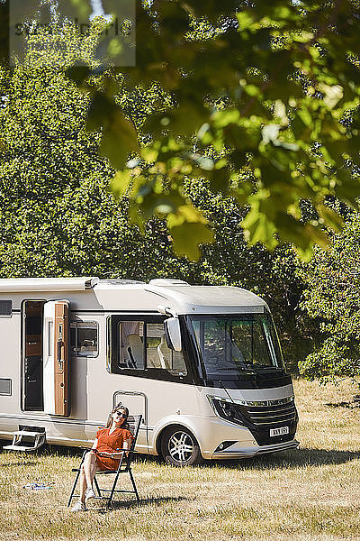 Reife Frau entspannt auf Stuhl gegen Wohnmobil auf Wohnwagenpark