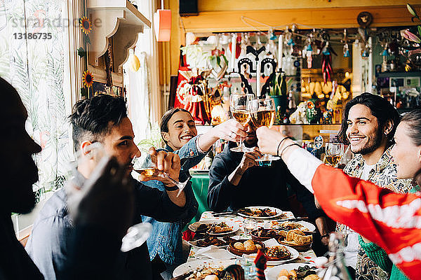 Junge multiethnische Freunde genießen es  bei Tisch im Restaurant anzustoßen