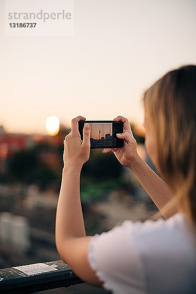 Ausschnitt einer jungen Frau  die bei Sonnenuntergang mit einem Smartphone den Fernsehturm fotografiert