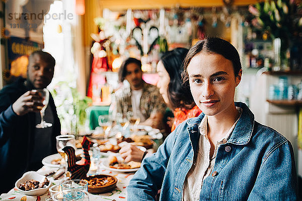 Porträt einer selbstbewussten jungen Frau  die während der Dinnerparty im Restaurant gegen Freunde am Tisch sitzt