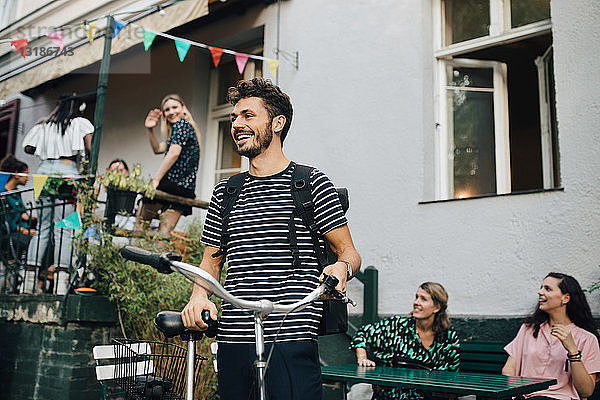 Lächelnder junger Mann steht mit Fahrrad im Hinterhof
