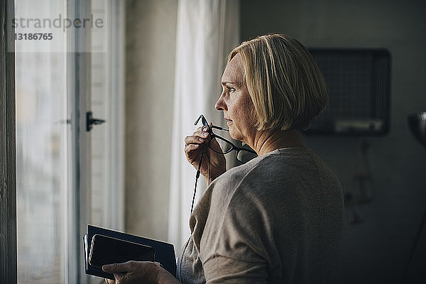 Reife Geschäftsfrau spricht über Kopfhörer  während sie im Kreativbüro am Fenster steht