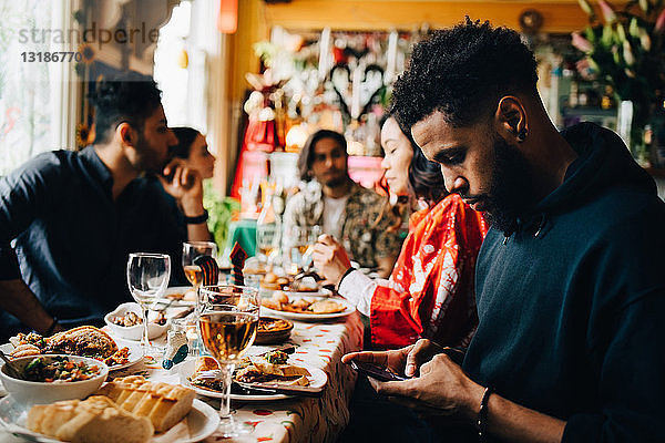 Junger Mann verschickt Textnachrichten über Smartphone  während er mit Freunden während einer Brunch-Party im Restaurant sitzt