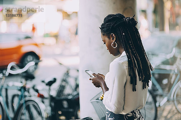 Junge Frau benutzt ein Smartphone  während sie in der Stadt auf einem Fußweg steht