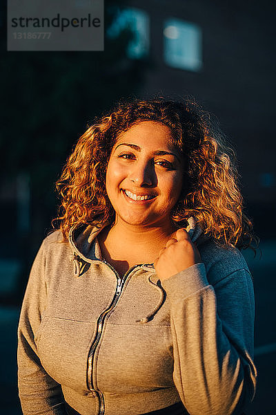 Porträt einer lächelnden jungen Frau mit Kapuzenshirt bei Sonnenuntergang