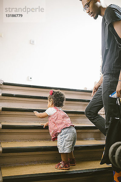 Junger Mann betrachtet Tochter beim Treppensteigen in Wohnung