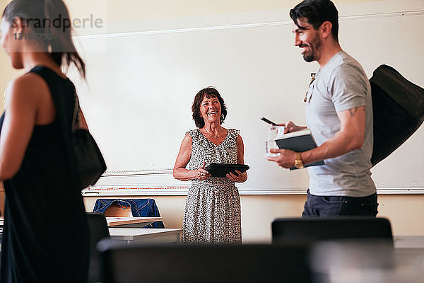 Ältere Frau lächelt  während sie ein digitales Tablet im Klassenzimmer hält