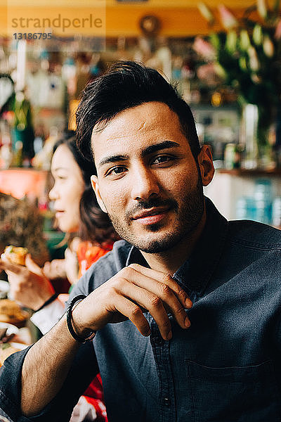 Porträt eines selbstbewussten jungen Mannes  der während einer Dinnerparty im Restaurant am Tisch sitzt