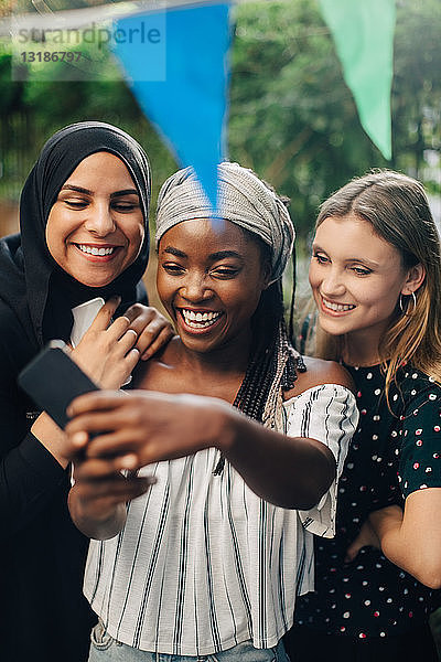 Glückliche multiethnische Freundinnen  die sich über ein Smartphone im Garten selbstständig machen
