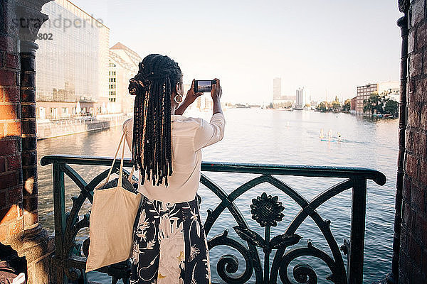 Rückansicht einer jungen Frau  die einen Fluss in der Stadt fotografiert
