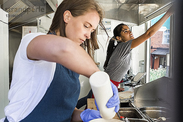 Selbstbewusste junge Besitzerin bereitet Essen zu  während ihre Kollegin im Speisewagen arbeitet
