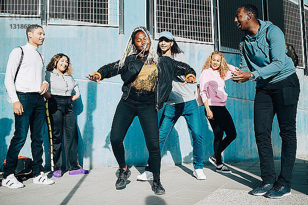 Lächelnde Freunde betrachten Teenager-Mädchen  die in der Stadt auf dem Bürgersteig tanzen