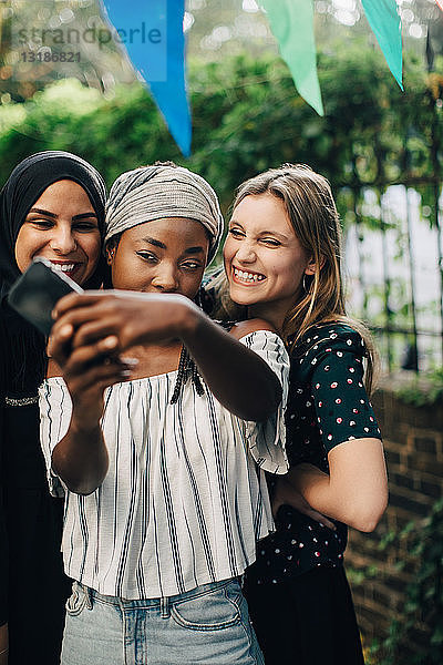 Fröhliche multiethnische Freundinnen  die sich im Hinterhof per Mobiltelefon selbstständig machen