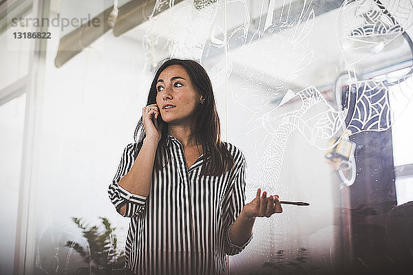 Kreative Geschäftsfrau schaut weg  während sie mit dem Handy gegen den Sitzungssaal telefoniert