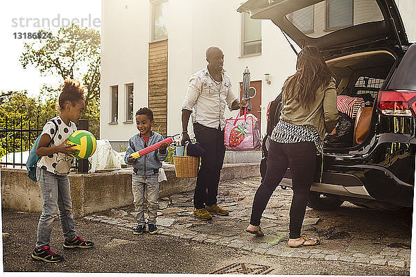 Familie in voller Länge mit Elektroauto auf Einfahrt gegen Haus