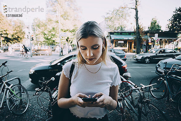 Junge Frau benutzt Mobiltelefon  während sie in der Stadt auf dem Bürgersteig steht
