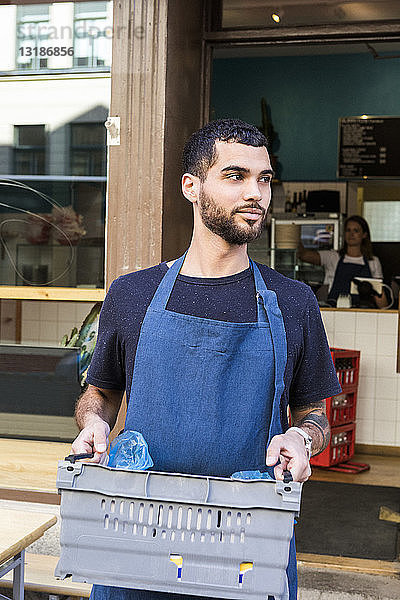 Selbstbewusster junger männlicher Besitzer trägt Kiste gegen Restaurant