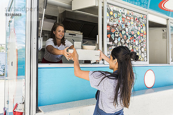 Lächelnde junge multiethnische Besitzerin übergibt Container an Verkäuferin am Speisewagen
