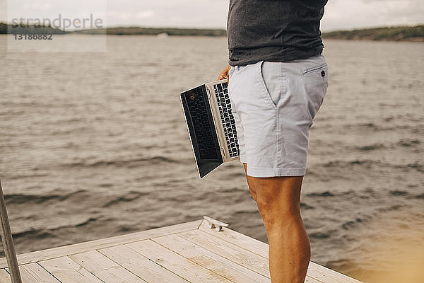 Ein Mann mit einem Laptop in der Hand  während er auf dem Steg über dem See steht