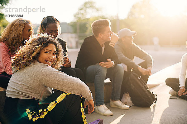 Porträt einer lächelnden jungen Frau  die mit Freunden im Skateboard-Park sitzt
