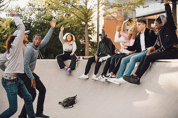 Freunde tanzen mit erhobenen Händen im Skateboard-Park
