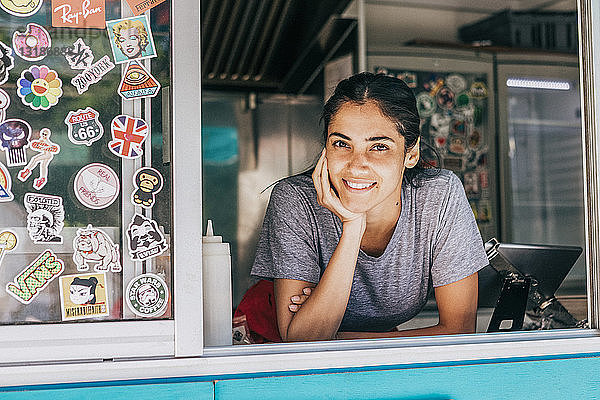 Porträt einer lächelnden jungen Verkäuferin  die sich am Fenster eines Speisewagens anlehnt