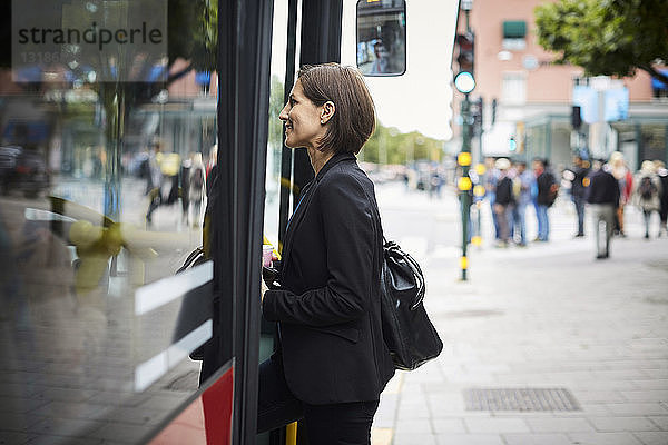 Seitenansicht einer lächelnden Geschäftsfrau  die in der Stadt in den Bus steigt