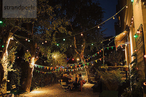 Multiethnische Freunde genießen Dinnerparty im beleuchteten Hinterhof
