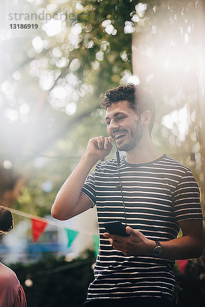 Glücklicher junger Mann spricht durch Kopfhörer  während er während der Party auf dem Balkon steht