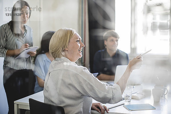 Lächelnde Geschäftsfrau zeigt während einer Sitzung mit Kollegen im Sitzungssaal