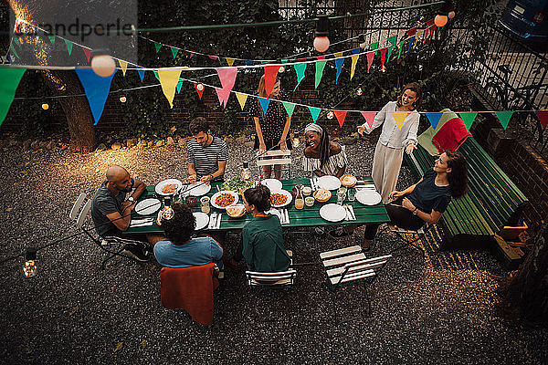Schrägansicht auf multiethnische Freunde  die während einer Gartenparty am Tisch zu Abend essen