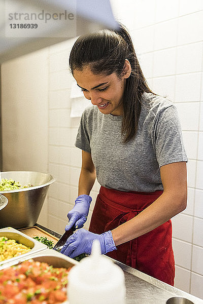 Lächelnder junger Küchenchef beim Zerkleinern von Speisen in der Großküche eines Restaurants