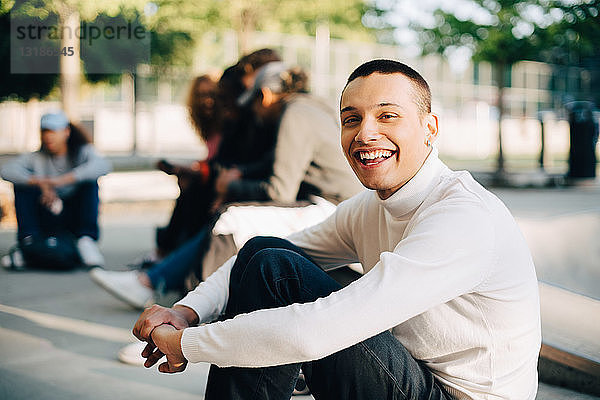 Porträt eines glücklichen jungen Mannes  der mit Freunden im Skateboard-Park sitzt
