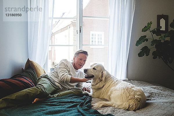 Älterer Mann streichelt Hund  während er sich zu Hause ans Bett lehnt
