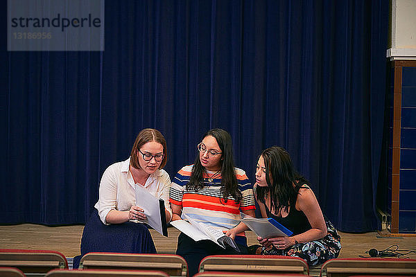 Multi-ethnische Frauen diskutieren über Notenblätter im Auditorium