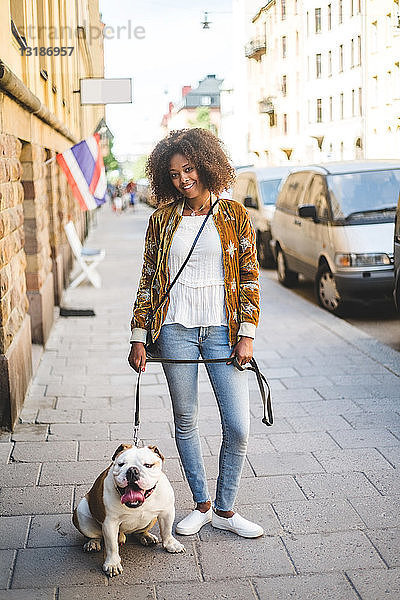 Porträt einer lächelnden  mittelgroßen  erwachsenen Frau mit Hund auf dem Bürgersteig in der Stadt
