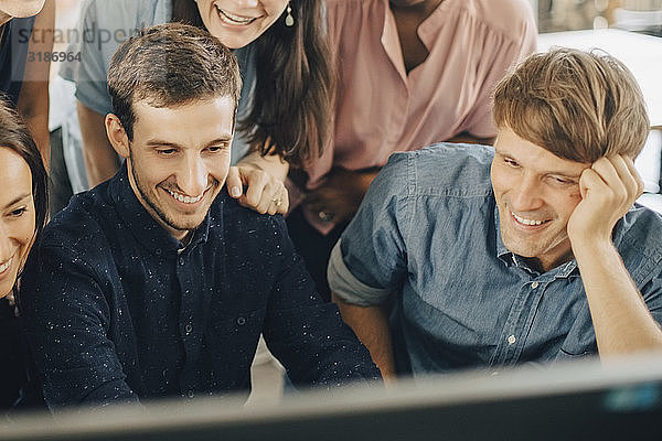 Lächelnde kreative Geschäftsleute  die während einer Besprechung im Büro auf den Computermonitor schauen