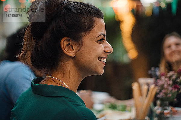 Lächelnde junge Frau schaut während einer Dinnerparty im Hinterhof weg