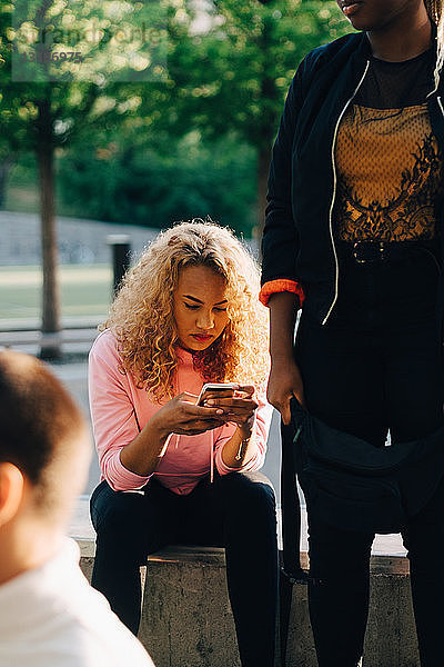 Junge Frau mit Freunden benutzt Smartphone im Park
