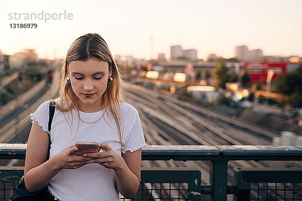 Junge Frau benutzt ein Smartphone  während sie auf einer Brücke in der Stadt steht