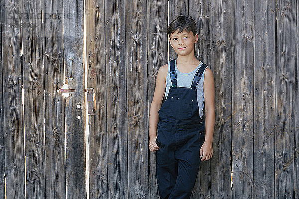 Porträt selbstbewusster Junge in Latzhose am Holzzaun