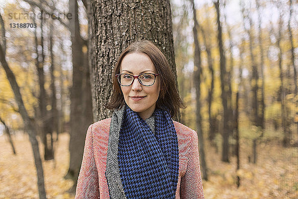 Porträt einer selbstbewussten Frau mit Schal  die im Herbst in einem Park vor einem Baum steht